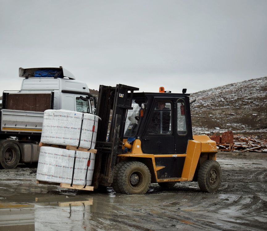 Real photograph of a forklift carrying a pallet beside a truck
